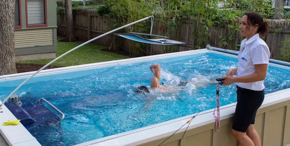 Person swimming in a small above-ground pool with an instructor monitoring beside the pool.