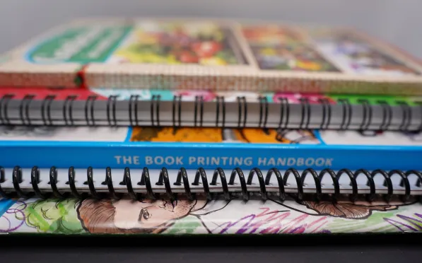 Close-up of spiral-bound books stacked, featuring colorful covers and a visible title The Book Printing Handbook.