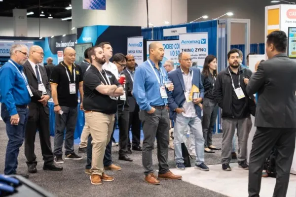 Group of professionals listening to a speaker at a technology trade show or conference booth