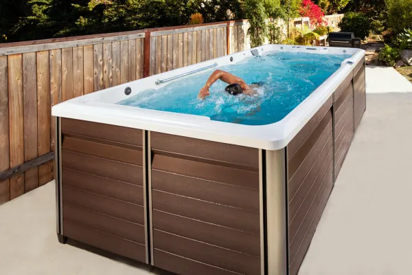 Person swimming in a modern rectangular outdoor swim spa with wood panel design beside a wooden fence.
