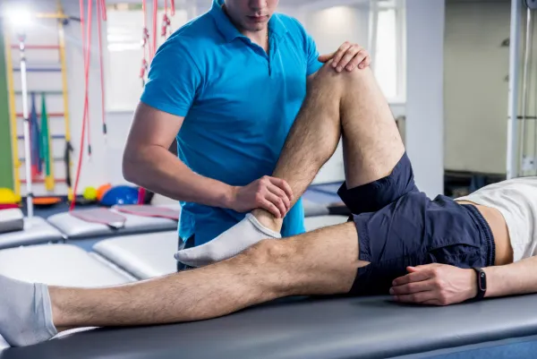 Physical therapist assists patient with leg stretching exercise on treatment table in a rehab clinic.