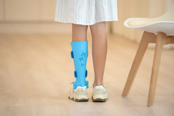 Child with a blue leg brace featuring butterfly designs wearing white sneakers on a wooden floor.