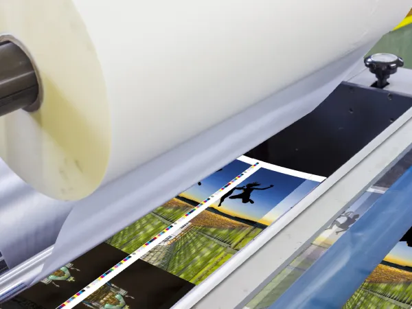 Large printer producing colorful photo prints including a sunset jump silhouette and landscape images.