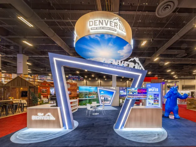 Modern Denver tourism booth with illuminated angular frame and promotional screens at indoor expo