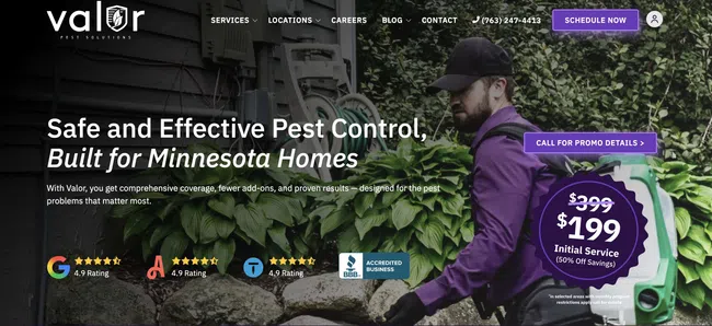 Pest control technician in purple gear sprays insecticide near home foundation surrounded by green plants.