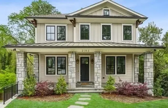 Two-story modern house with stone pillars, black-framed windows, and a manicured lawn with stepping stones.