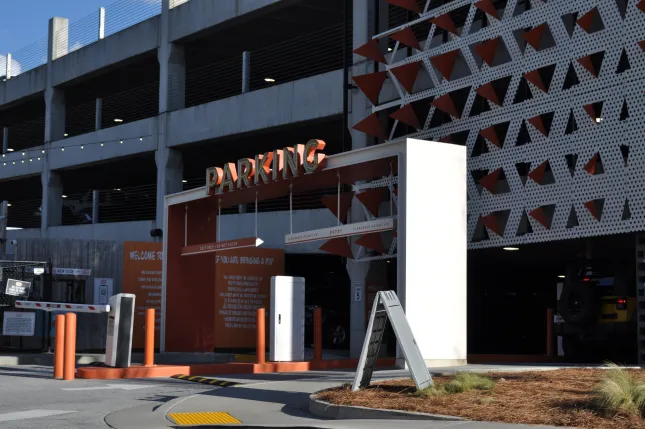 Entrance to a modern multi-level parking garage with orange and white signage and geometric facade patterns.