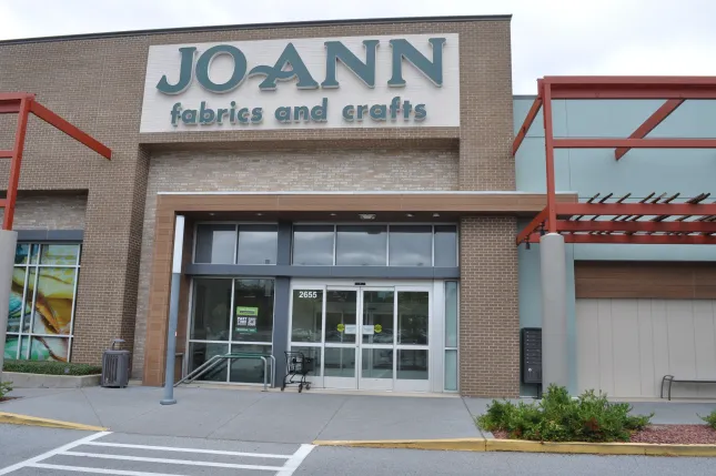 Jo-Ann Fabrics and Crafts store exterior with entrance, signage, and parking area visible on a cloudy day