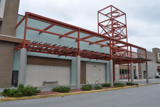 Empty storefront with red steel awning and pillars in a shopping center on a cloudy day
