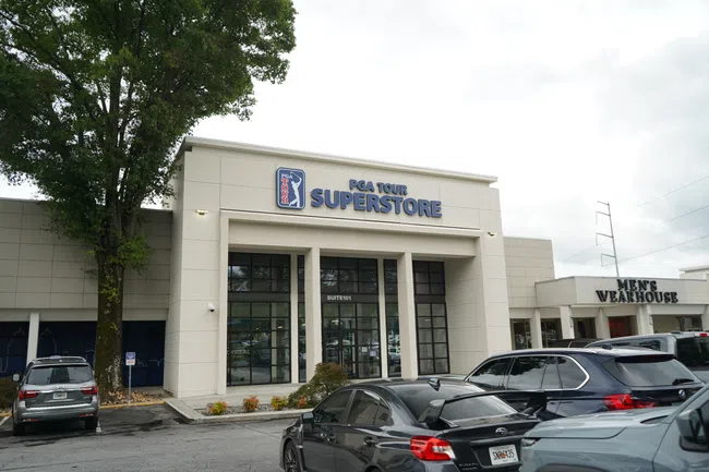 Exterior view of PGA Tour Superstore with cars parked in front and Men's Wearhouse adjacent.