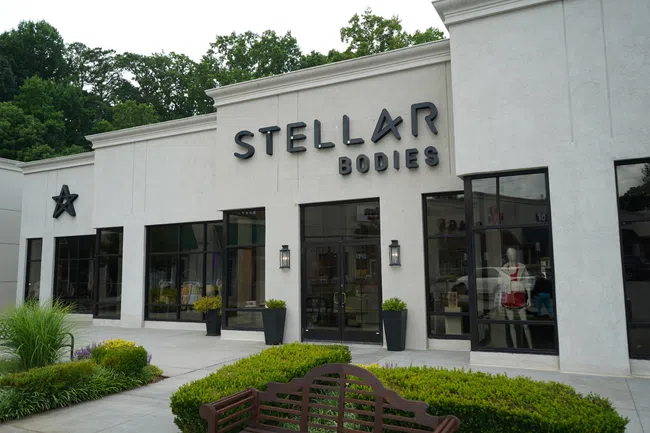 Exterior view of Stellar Bodies fitness studio with modern signage and large windows surrounded by greenery