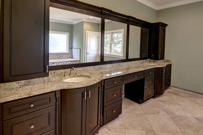 Luxury bathroom vanity with dark wood cabinets, marble countertop, large mirror, and tiled floor under natural light.