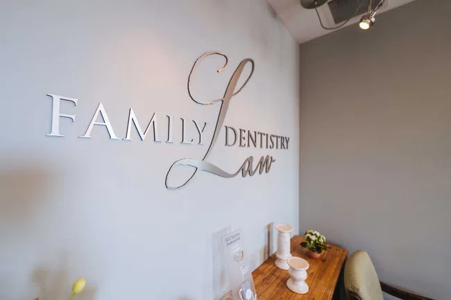 Modern dental office wall sign reading Family Dentistry Law with wooden table and decorations inside clinic.