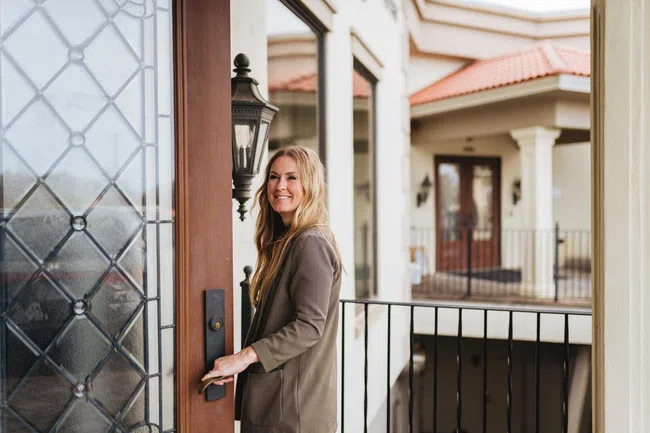 Smiling woman opening a front door with stained glass on a sunny day at a residential building