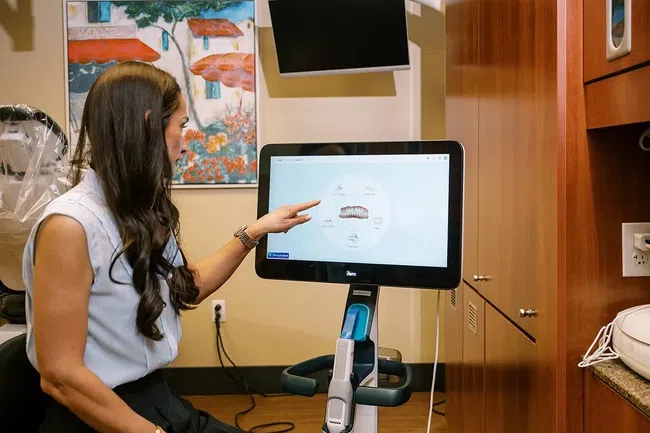 Woman in dental office pointing at a 3D dental scan on a large touchscreen display.