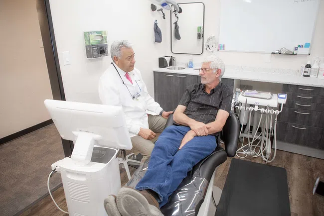 Dentist consulting with an elderly male patient seated in a dental chair in a modern clinic room.
