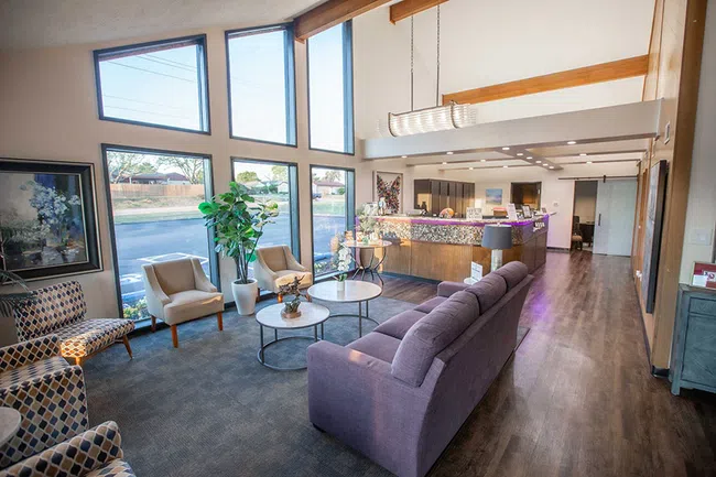 Bright modern waiting room with large windows, comfortable chairs, purple couch, and reception desk in background.