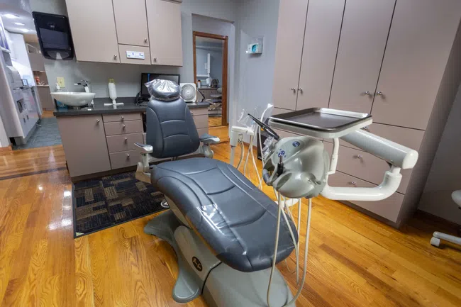 Modern dental clinic room with reclining dental chair, instrument tray, and wooden flooring.