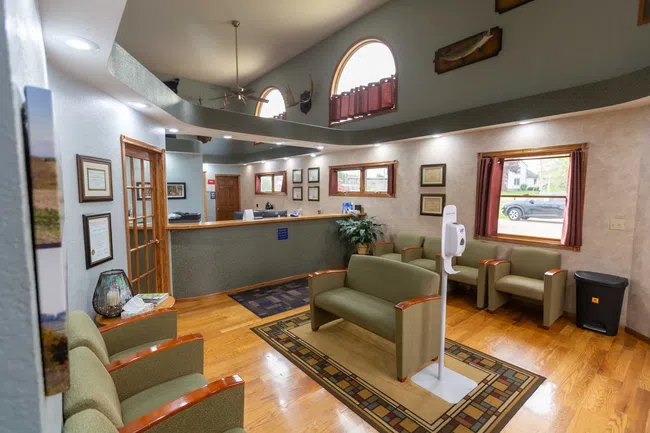 Bright medical office reception area with green seating, wood floors, large windows, and high arched ceiling.