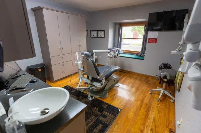 Modern dental clinic room with dental chair, sink, monitors, cabinets, and wooden flooring