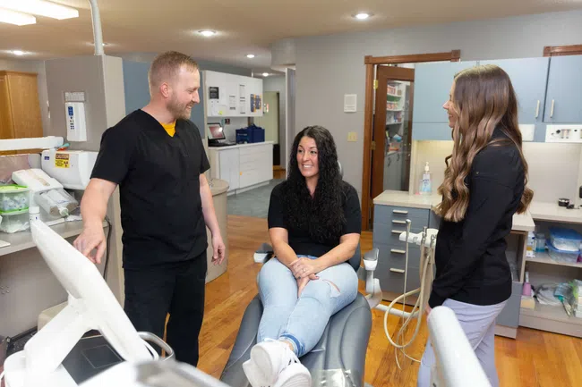 Dentist talking with female patient sitting in dental chair and dental assistant standing nearby in clinic