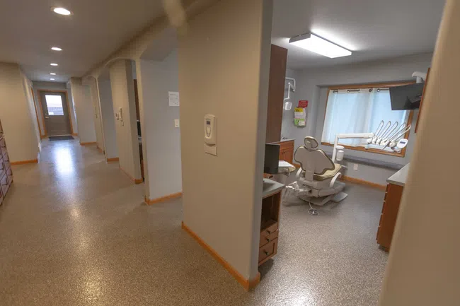 Bright dental clinic corridor leading to a treatment room with dental chair and equipment by a window.