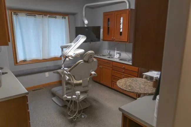 Modern dental office with a dental chair, equipment, wooden cabinets, and a window with curtains.
