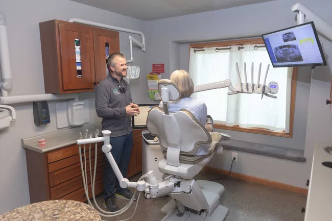 Dentist explaining dental X-rays on screen to patient seated in modern dental chair in clinic room.
