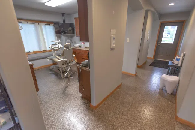 Modern dental clinic room with dental chair, equipment, wooden cabinets, and a clean hallway with natural light.