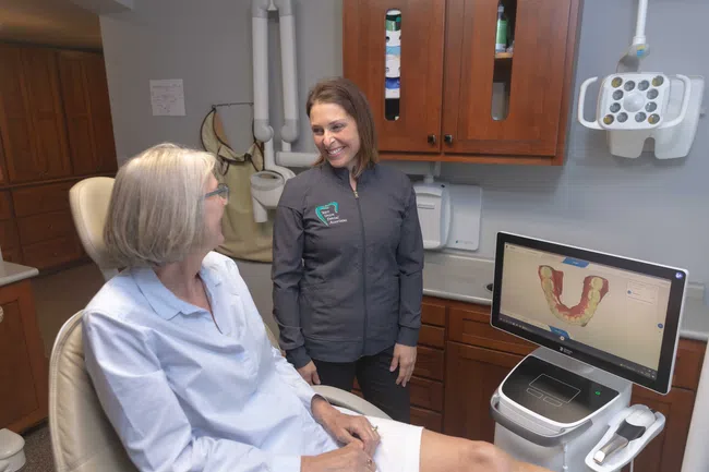 Dentist consulting female patient in a dental office with 3D dental scan shown on monitor.