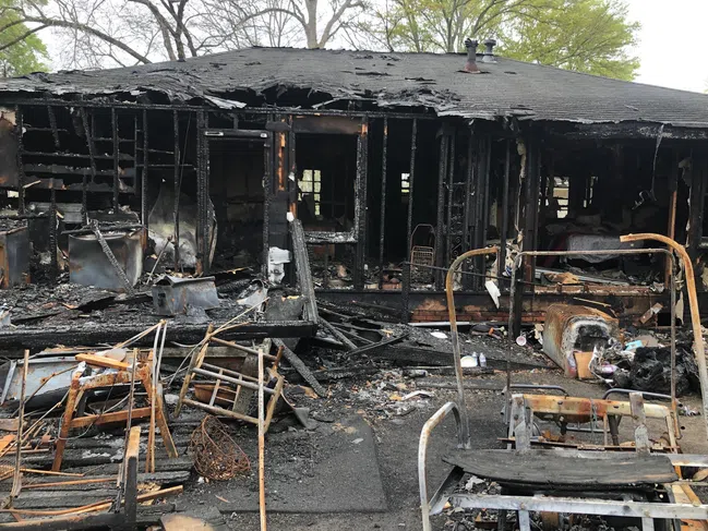 Burned house with charred walls and destroyed furniture after a severe fire incident outdoors.