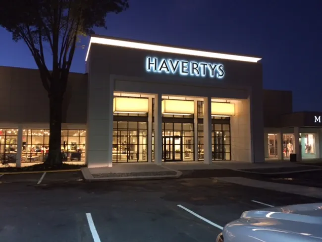 Havertys furniture store entrance illuminated at night with glass windows and empty parking spaces.
