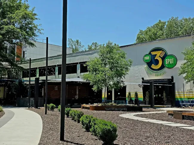 Outdoor view of 3rd Spot brewery and restaurant with trees, walkway, and seating under clear blue sky.