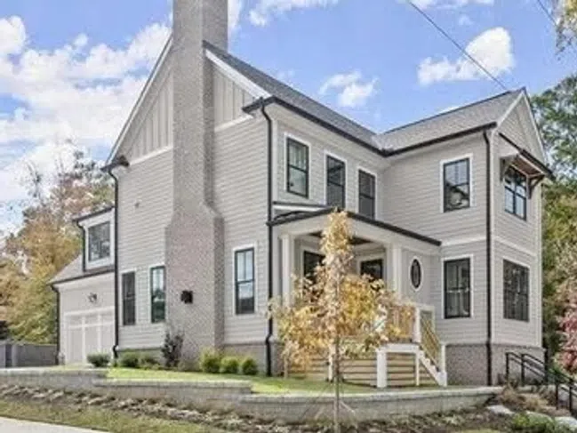Modern two-story white house with black window frames, front porch, and a large chimney on a sunny day