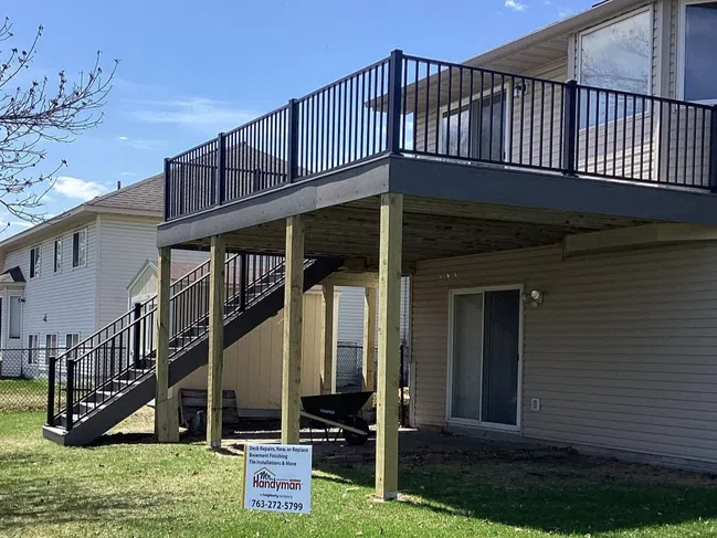 New elevated wooden deck with black metal railings attached to beige house with advertisement sign on green lawn.
