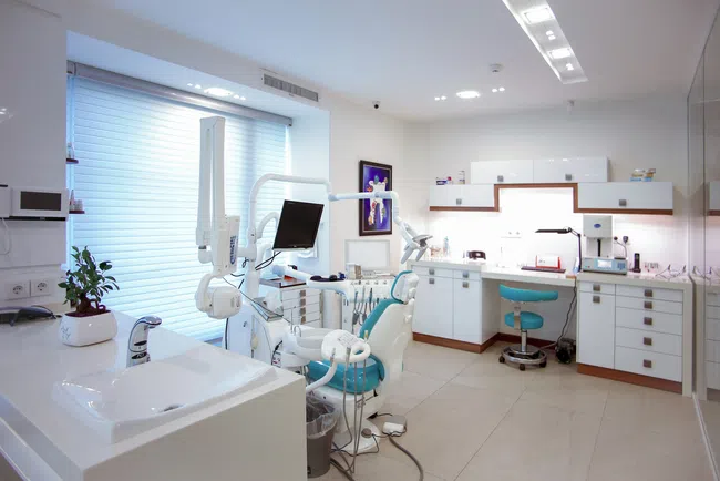 Bright modern dental clinic with dental chair, monitor, sink, and white cabinetry under natural light.