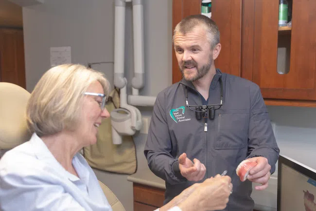 Dentist explaining dental care using a teeth model to a smiling older female patient in clinic.