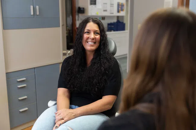 Smiling woman with long curly hair sitting and talking to another person in a modern office setting