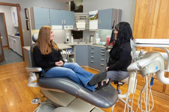 Patient and dental hygienist smiling and talking in a modern dental office with equipment and cabinets.