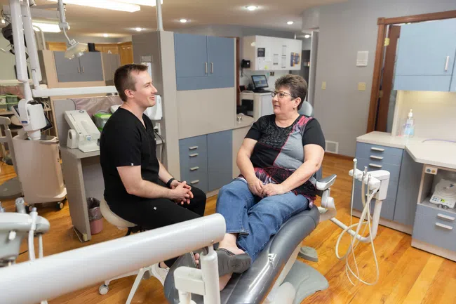 Dentist in black scrubs talking with female patient sitting on dental chair in modern clinic.