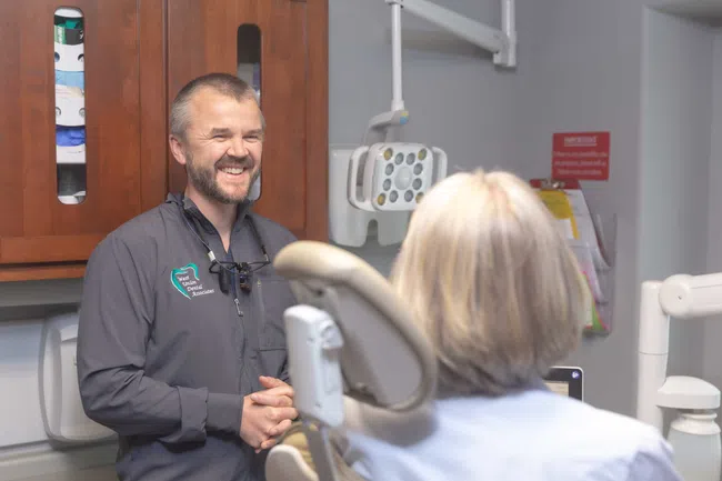 Dentist smiling and talking with a patient seated in a dental chair in a modern clinic room
