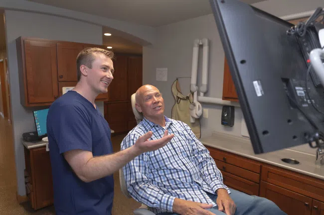 Dentist explaining dental X-ray results to elderly male patient in modern clinic office.