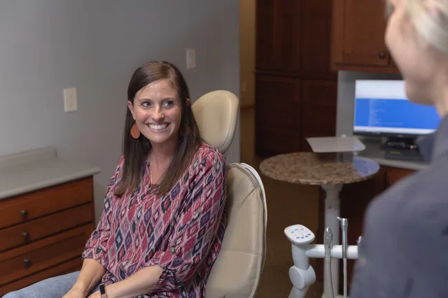 Smiling woman sitting in dental chair during consultation with dental professional in office.