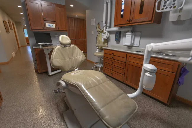 Modern dental clinic room with beige dental chair, wooden cabinets, and dental equipment.
