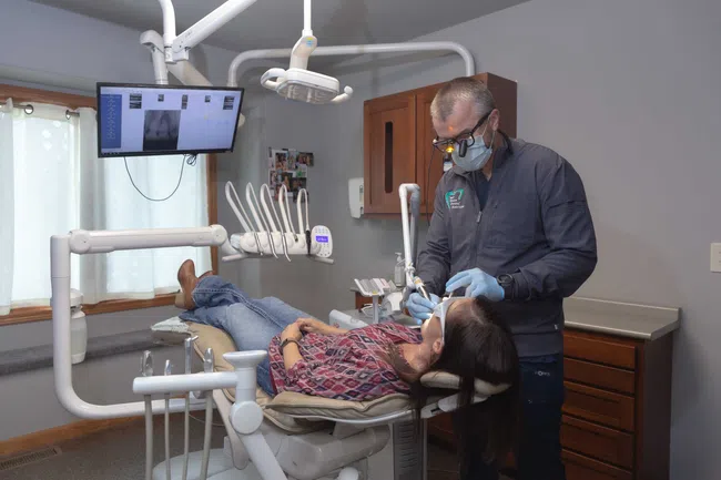Dentist wearing magnifying glasses treating a female patient reclining in dental chair in modern clinic.