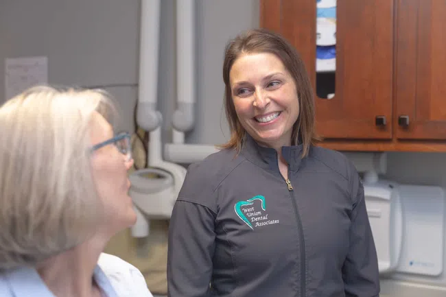 Dental professional smiling and talking with a female patient in a dental office setting.
