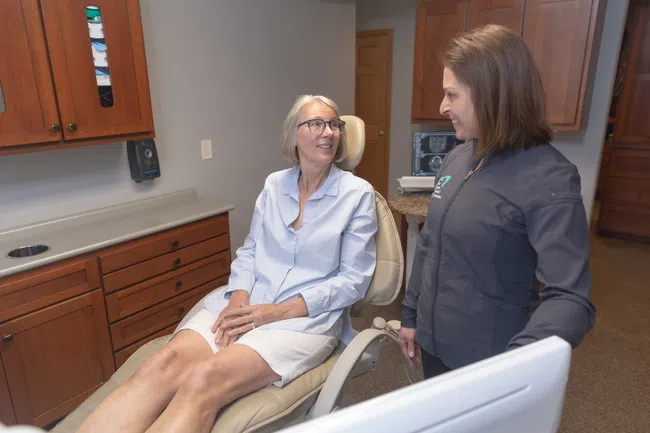 Senior woman patient sitting in a dental chair talking to a female dentist in a clinic room.