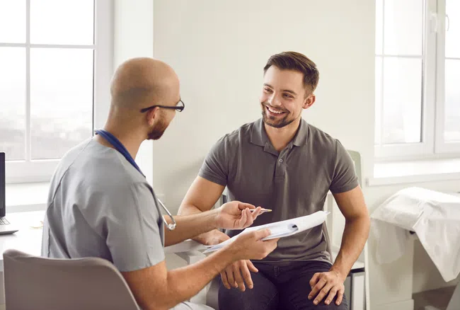 Doctor consulting a smiling male patient in a bright medical office discussing health information.