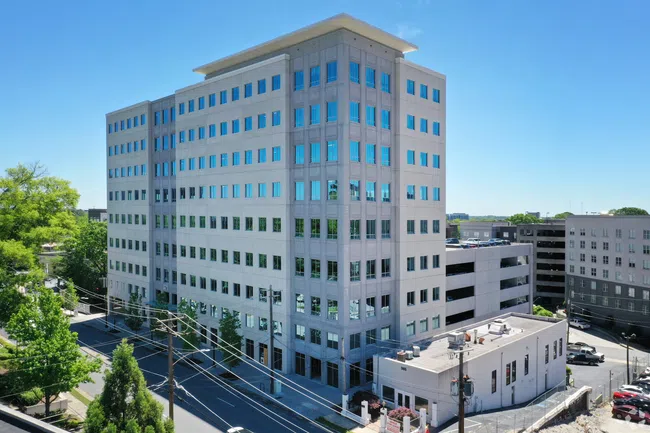 Modern multi-story office building with reflective windows under clear blue sky in an urban environment.