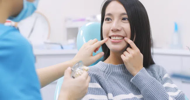 Dentist showing a woman how dental implants fit while she smiles in a dental clinic.